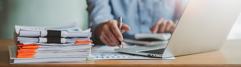 Man working at a desk with laptop and stacks of documents