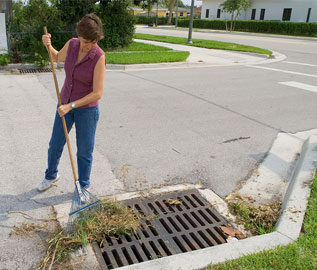 photo of woman clearing leaves from a drainage grate