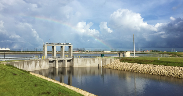 Water control structure along canal with grassy banks and a rainbow